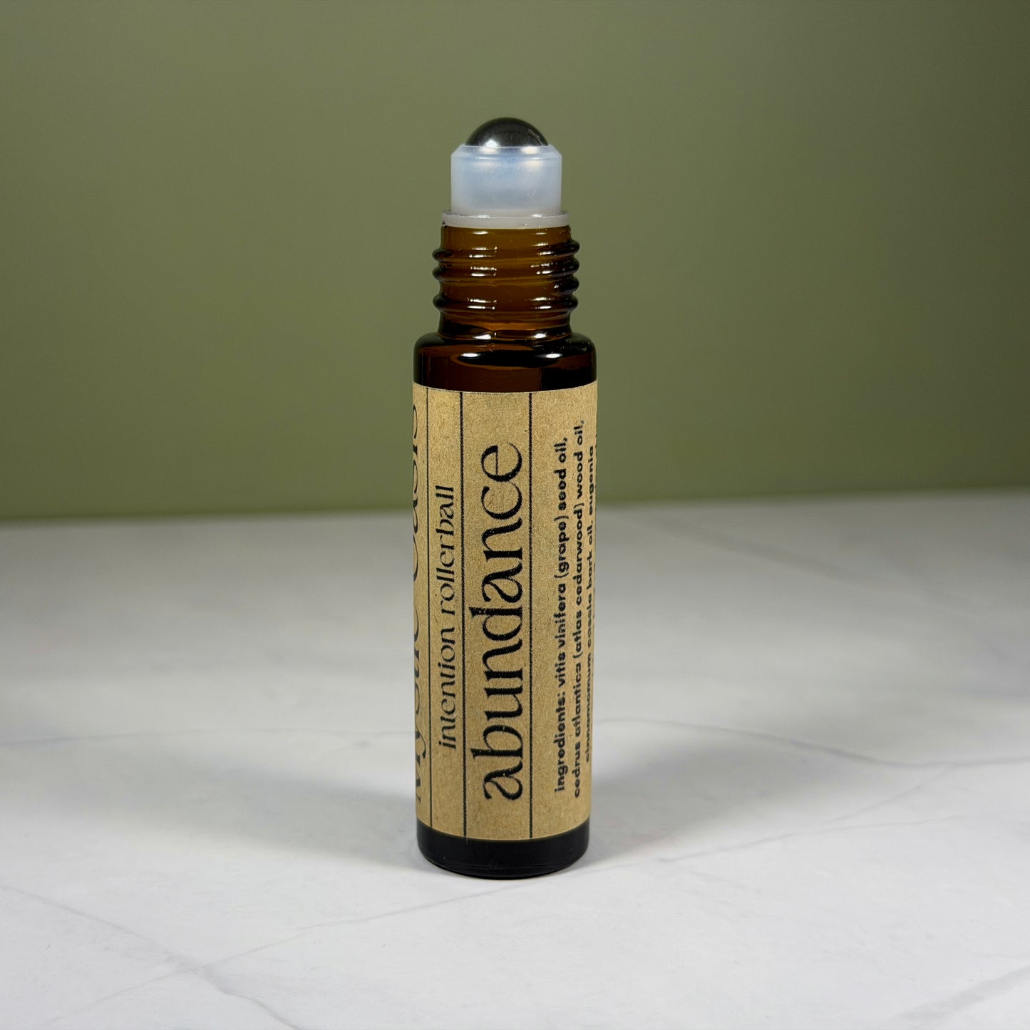 Roll-on bottle labeled 'abundance' on a white surface with a green background