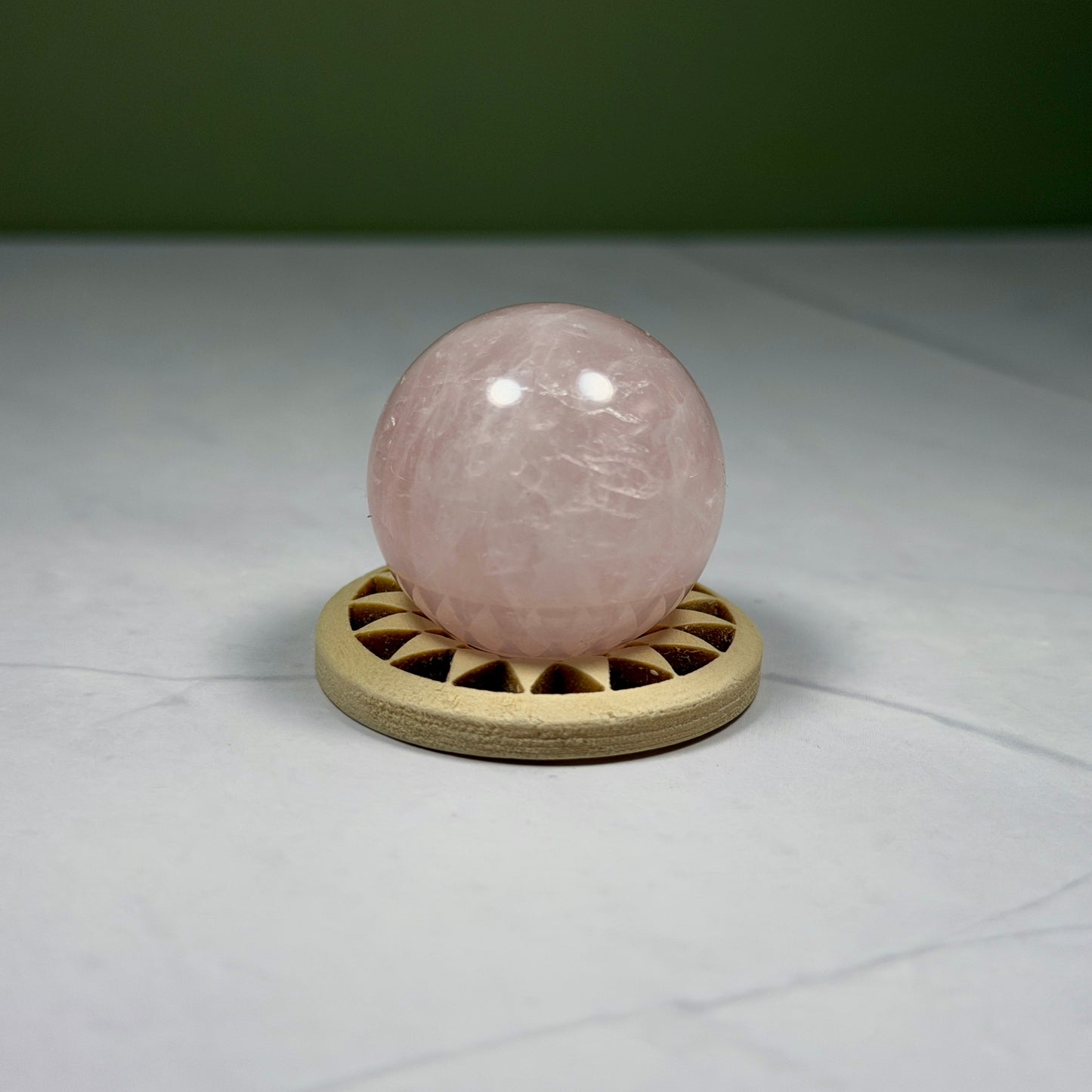 Rose quartz crystal ball on a wooden stand against a neutral background