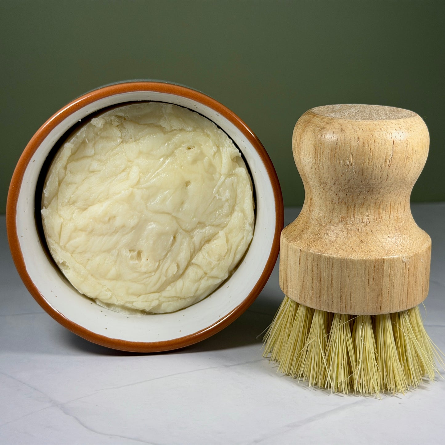 Wooden dish brush next to a bowl of soap on a gray surface.