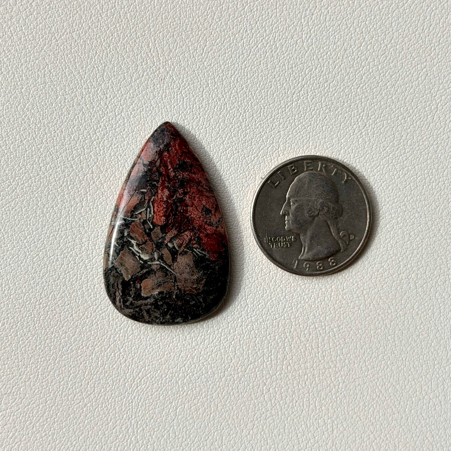 Teardrop-shaped stone next to a U.S. quarter on a light gray background
