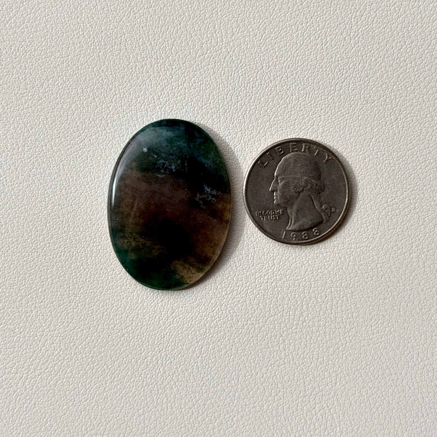 Oval-shaped dark stone next to a U.S. quarter on a light gray background