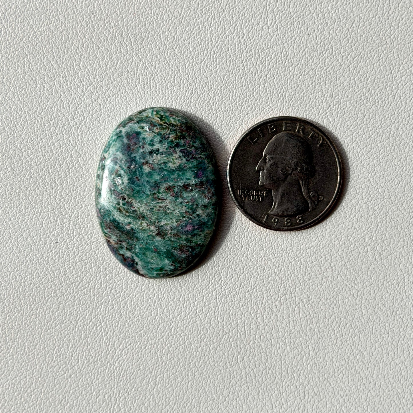 Oval-shaped green stone next to a penny on a light gray background