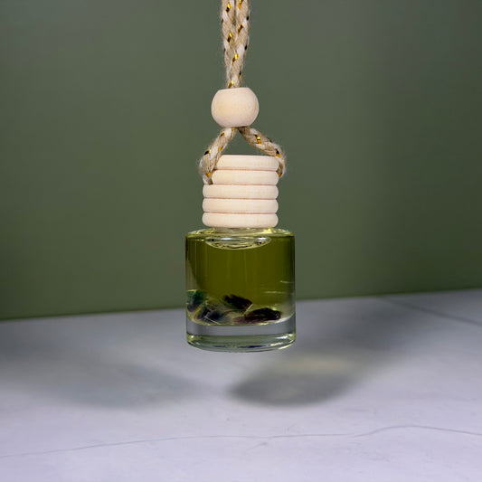 Glass diffuser bottle with wooden beads hanging against a green background