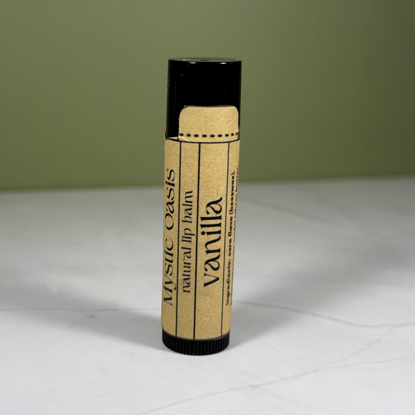 Vanilla-flavored lip balm with kraft packaging on a white surface and green background