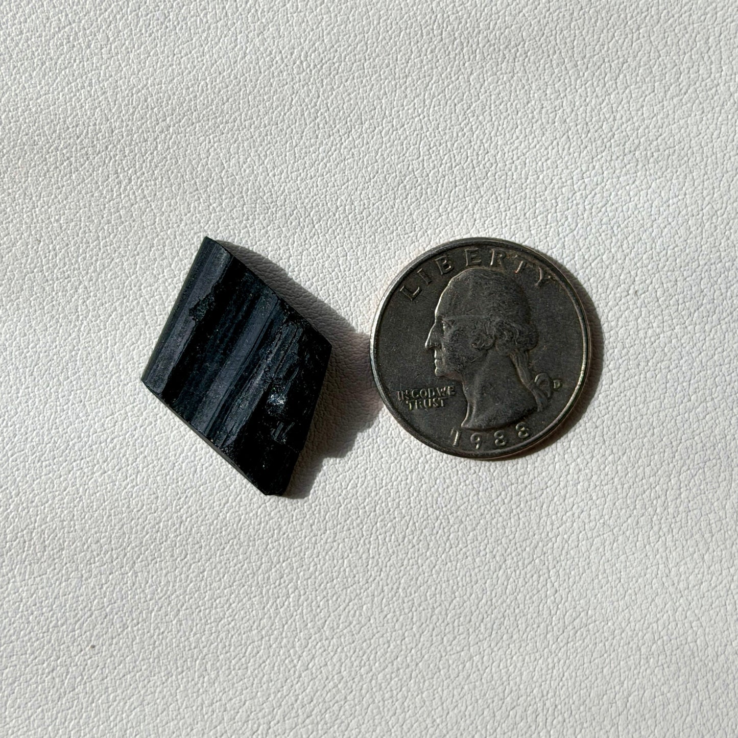 Black rectangular stone next to a U.S. quarter on a light gray background