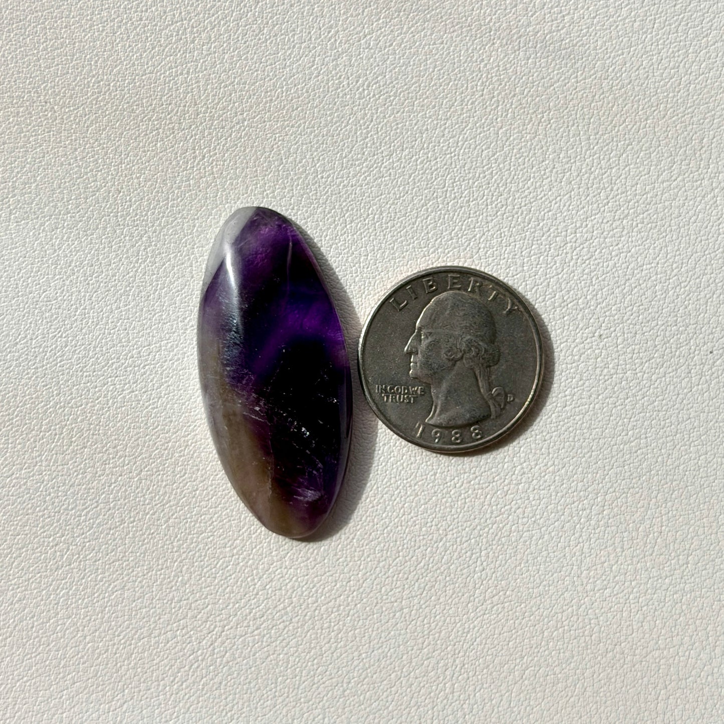 oval shaped Purple amethyst crystal next to a U.S. quarter on a white background