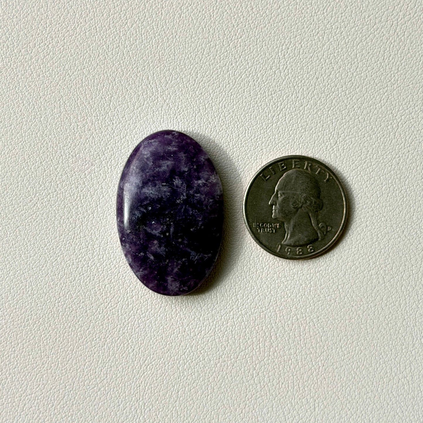 Purple oval stone next to a U.S. quarter on a light gray background