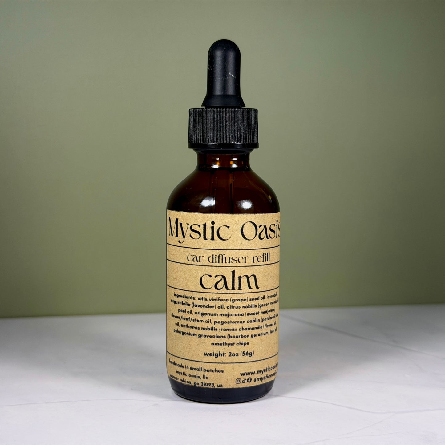 Brown glass bottle with dropper labeled 'Mystic Oasis calm' on a white surface with a green background