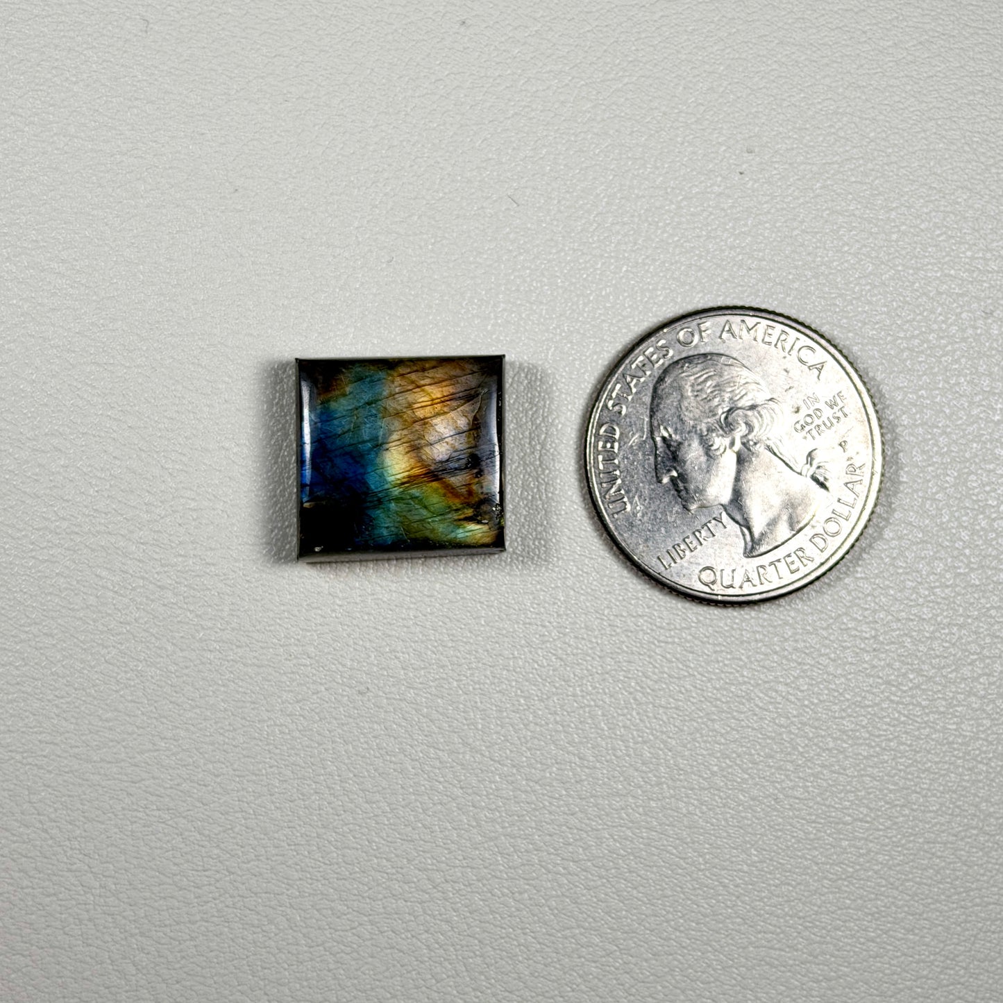 Colorful square labradorite stone next to a quarter on a gray background