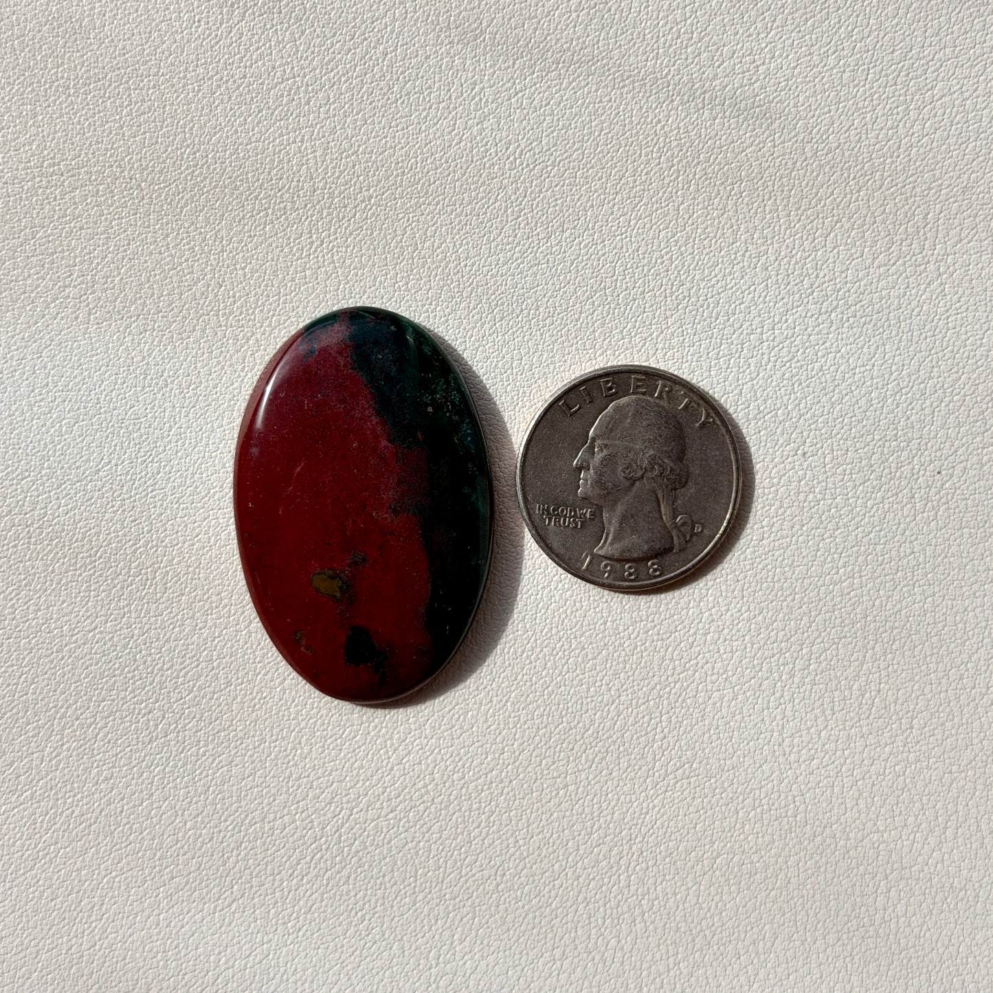 Oval red stone next to a U.S. quarter on a light gray background