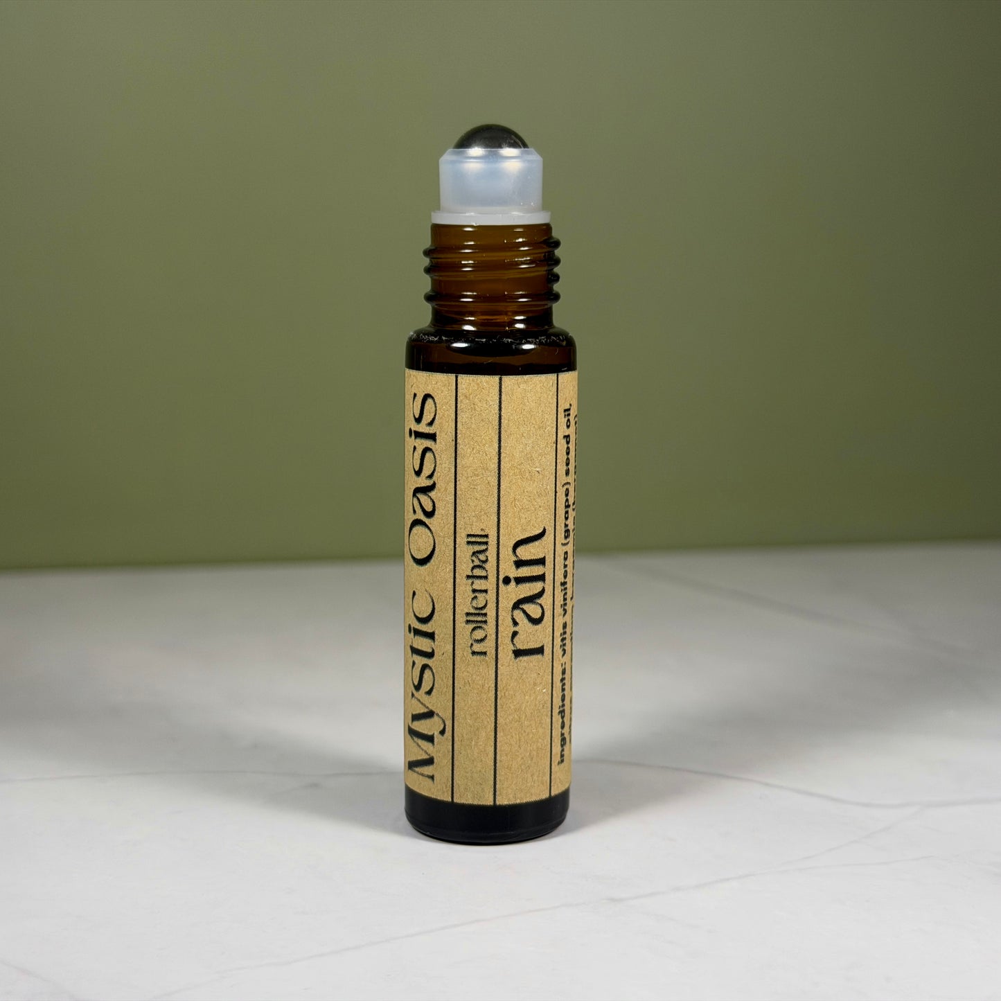 Rollerball bottle labeled 'Mystic Oasis Rain' on a light surface with a green background