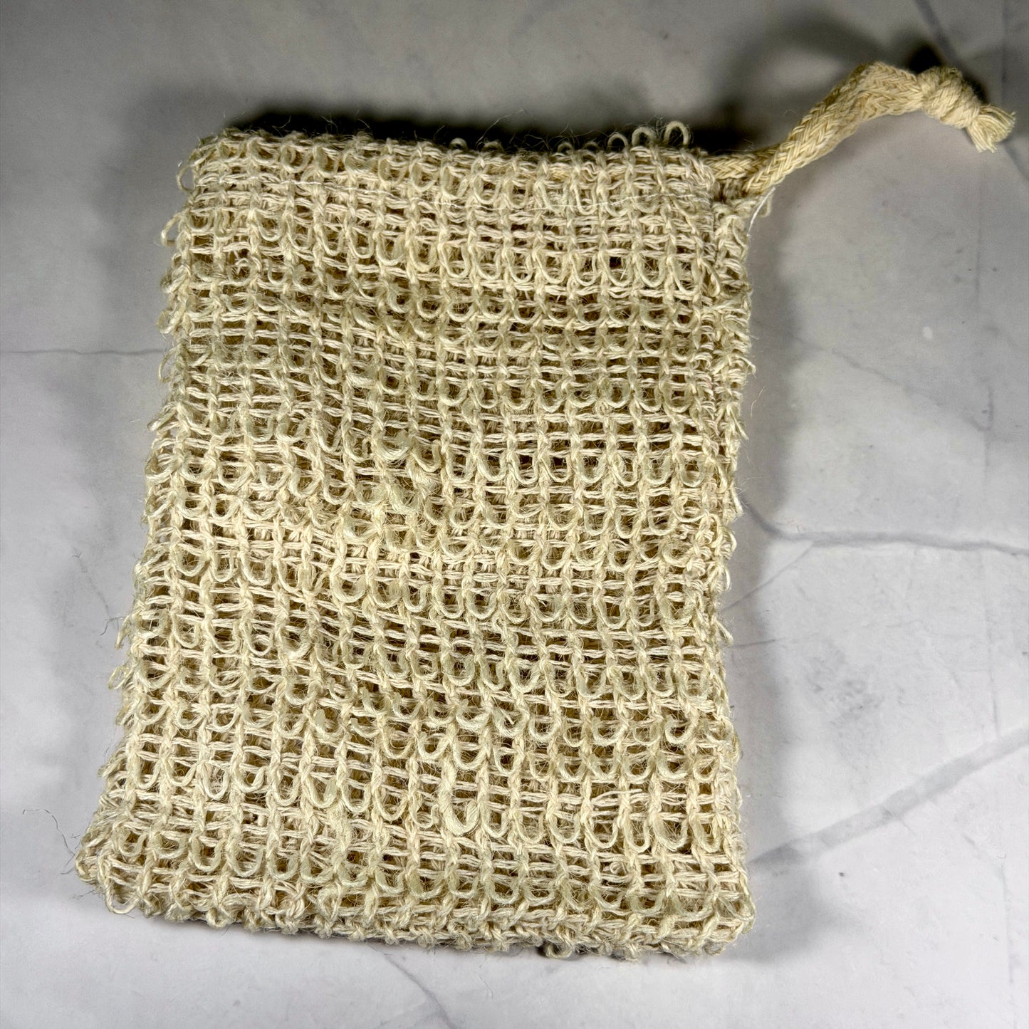 Beige woven soap scrubber on a marble surface