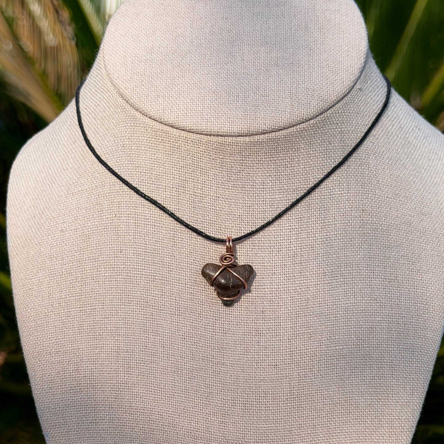 Necklace with a shark tooth pendant on a mannequin bust against a blurred natural background