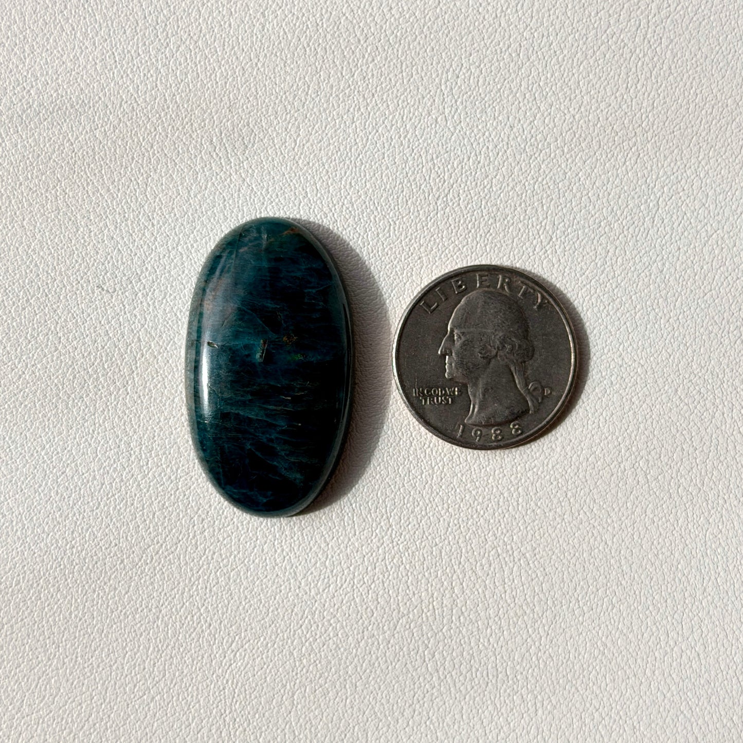 Blue oval stone next to a U.S. quarter on a light gray background