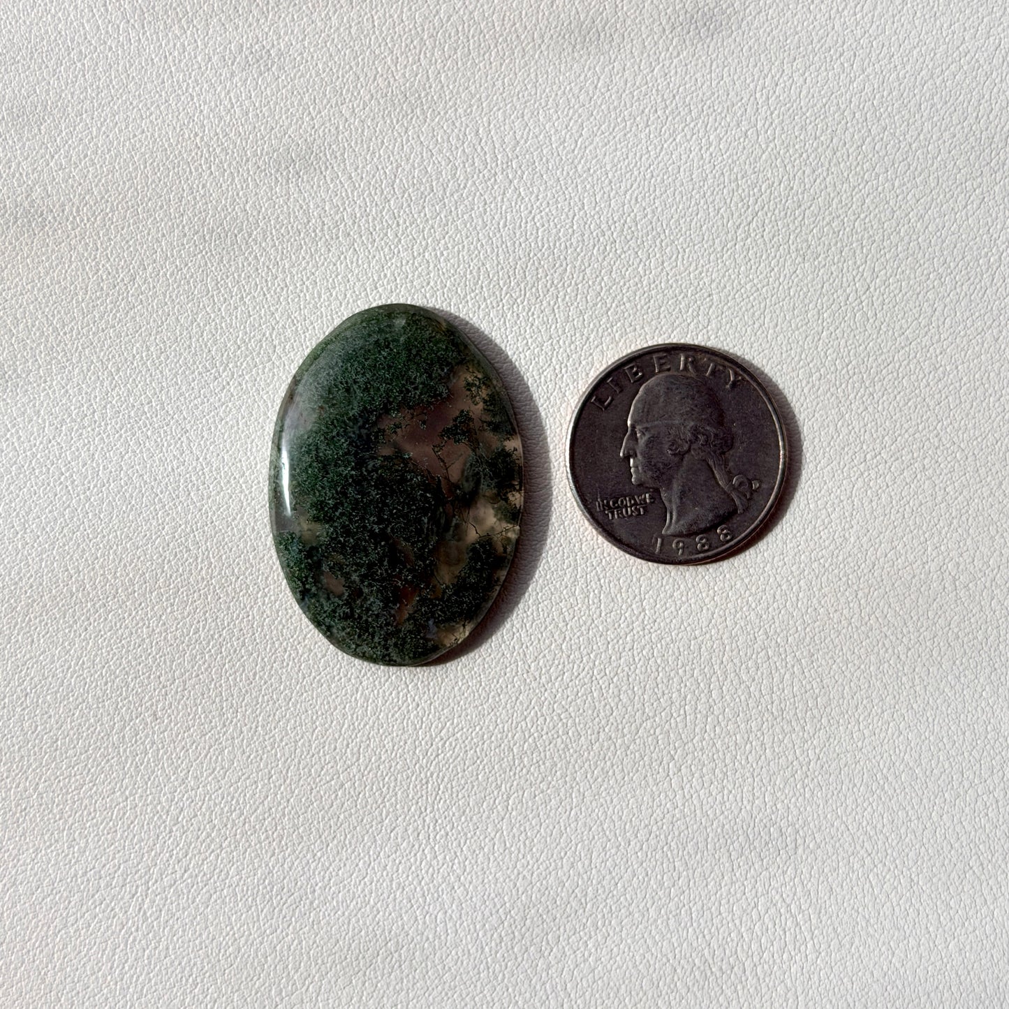 Oval-shaped green stone next to a U.S. quarter on a light gray background