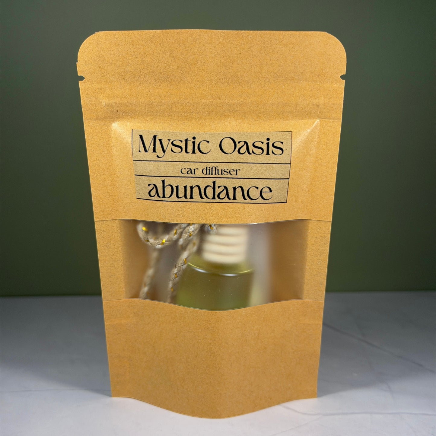 Kraft paper packaging with 'Mystic Oasis' car diffuser labeled 'abundance' on a green background.