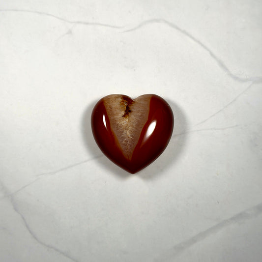 Heart-shaped red and white stone on a textured white surface