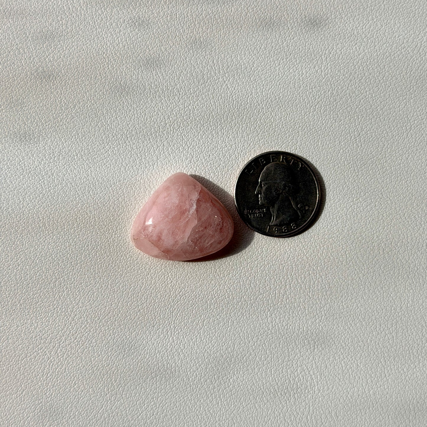 Pink stone next to a U.S. quarter on a light gray background
