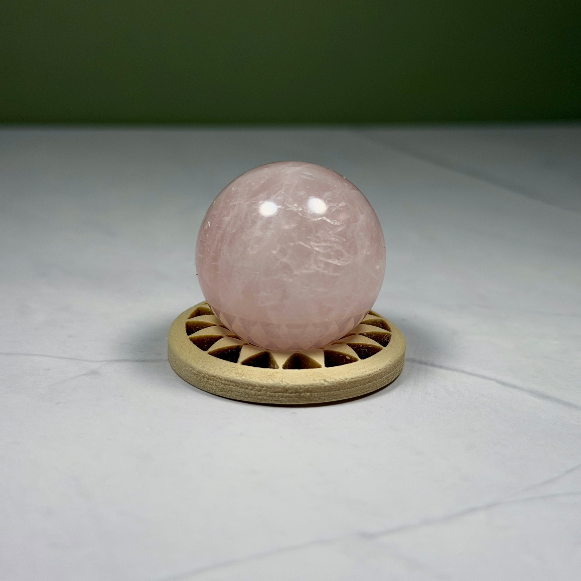 Rose quartz crystal ball on a wooden stand against a neutral background