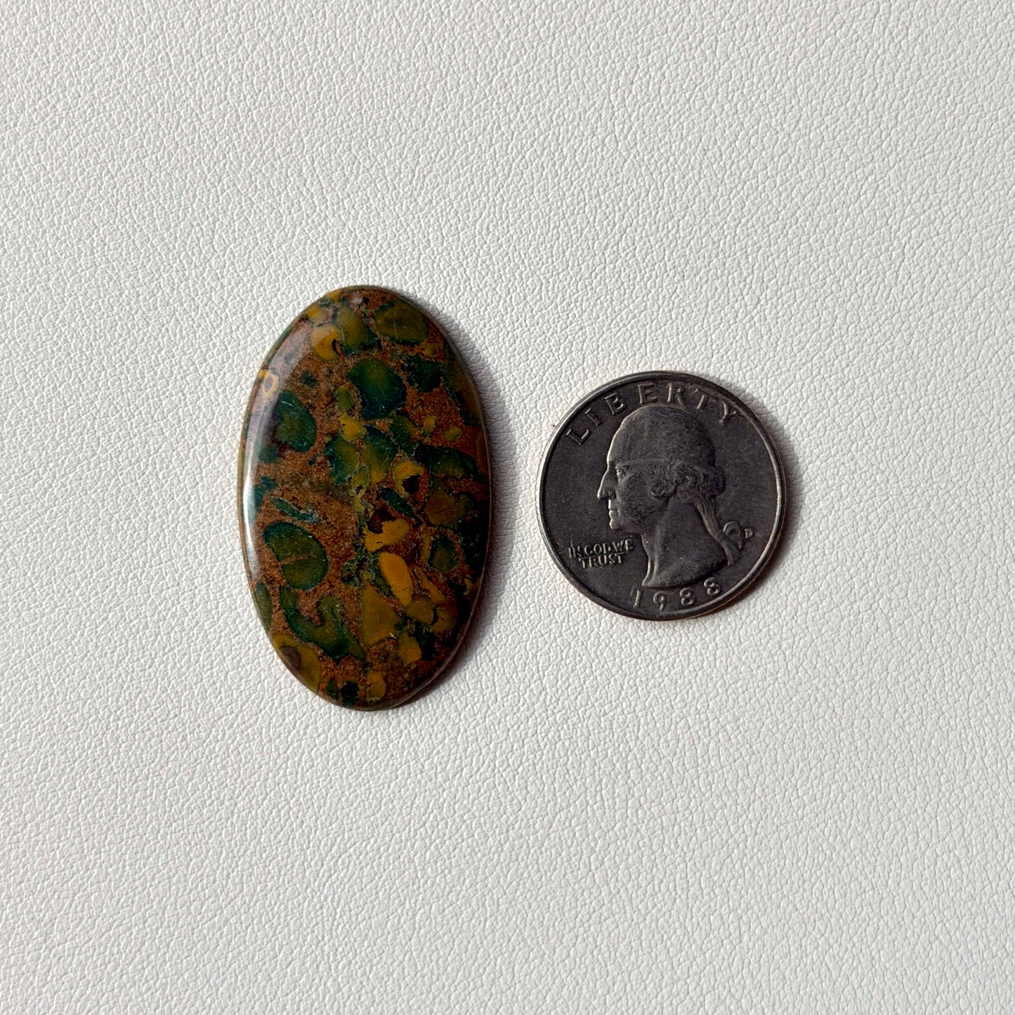 Oval-shaped multicolored stone next to a U.S. quarter on a white background