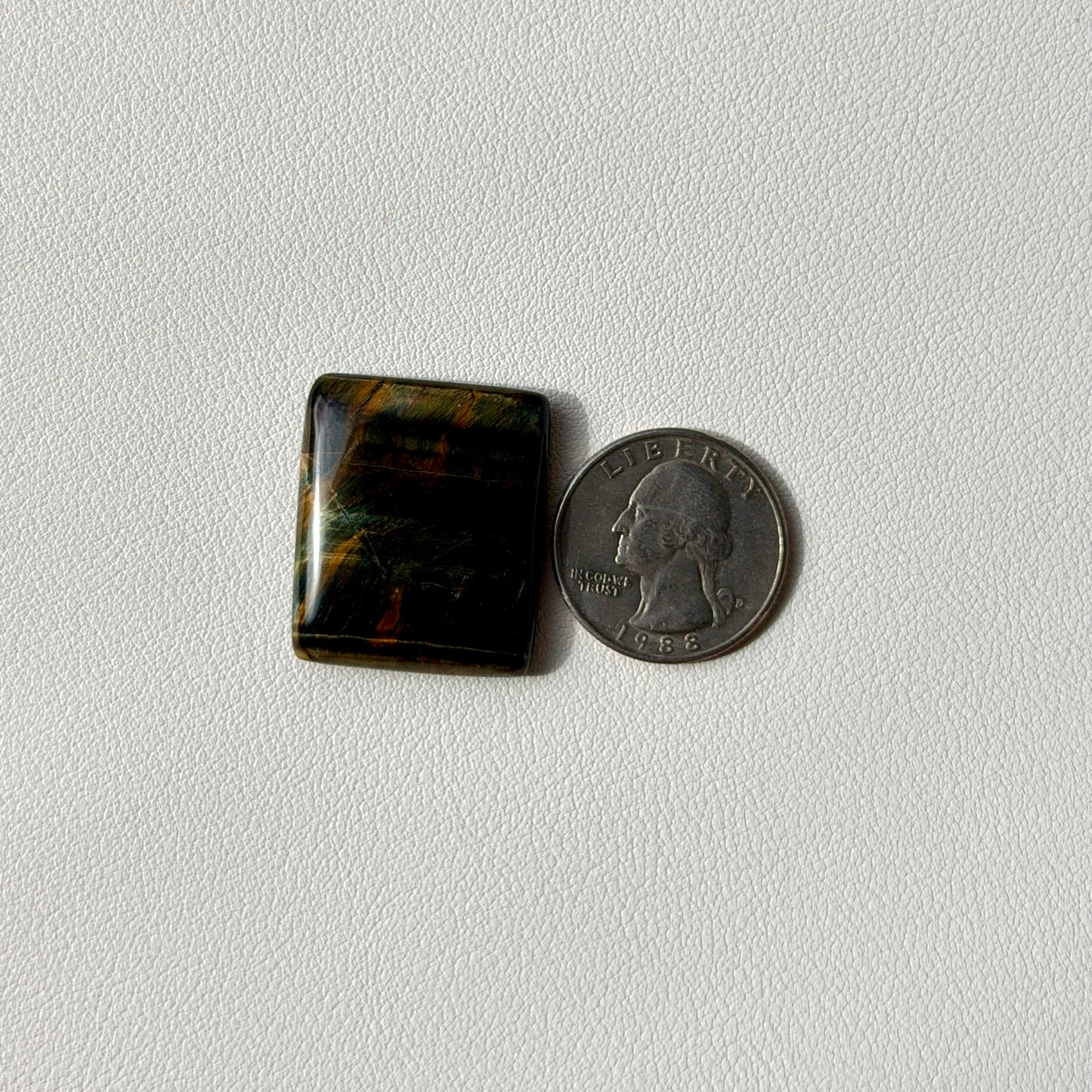 Square-shaped blue stone next to a U.S. quarter on a light gray background