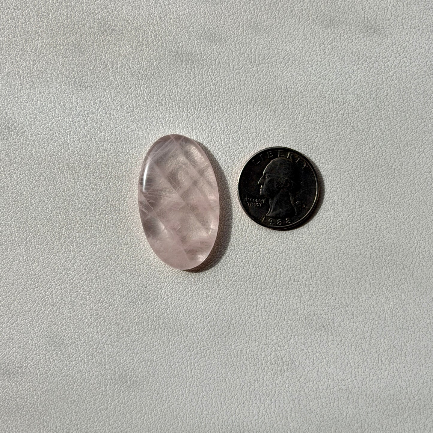 Oval-shaped rose quartz crystal next to a U.S. quarter on a light gray background