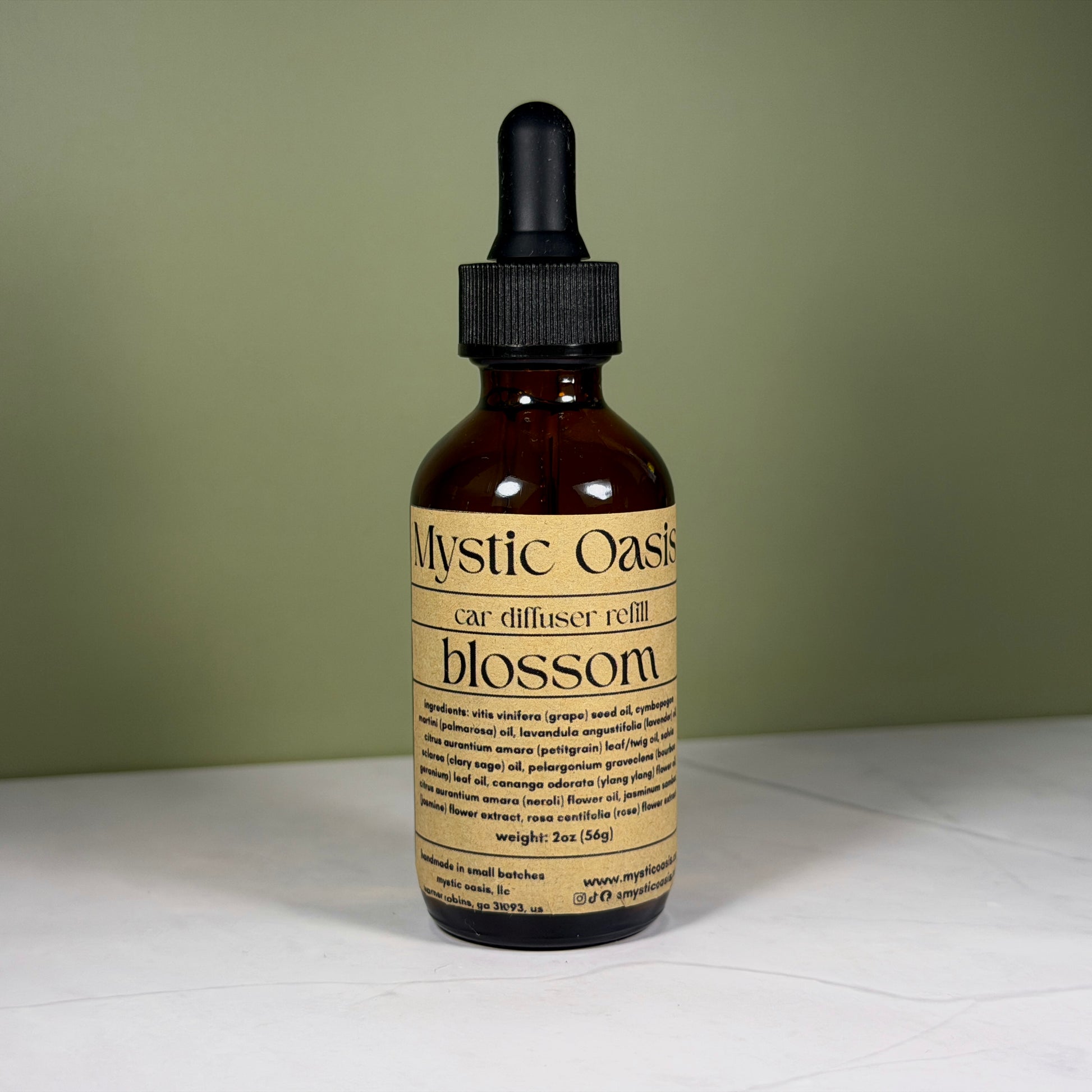 Mystic Oasis car diffuser refill bottle with dropper on a white surface and green background