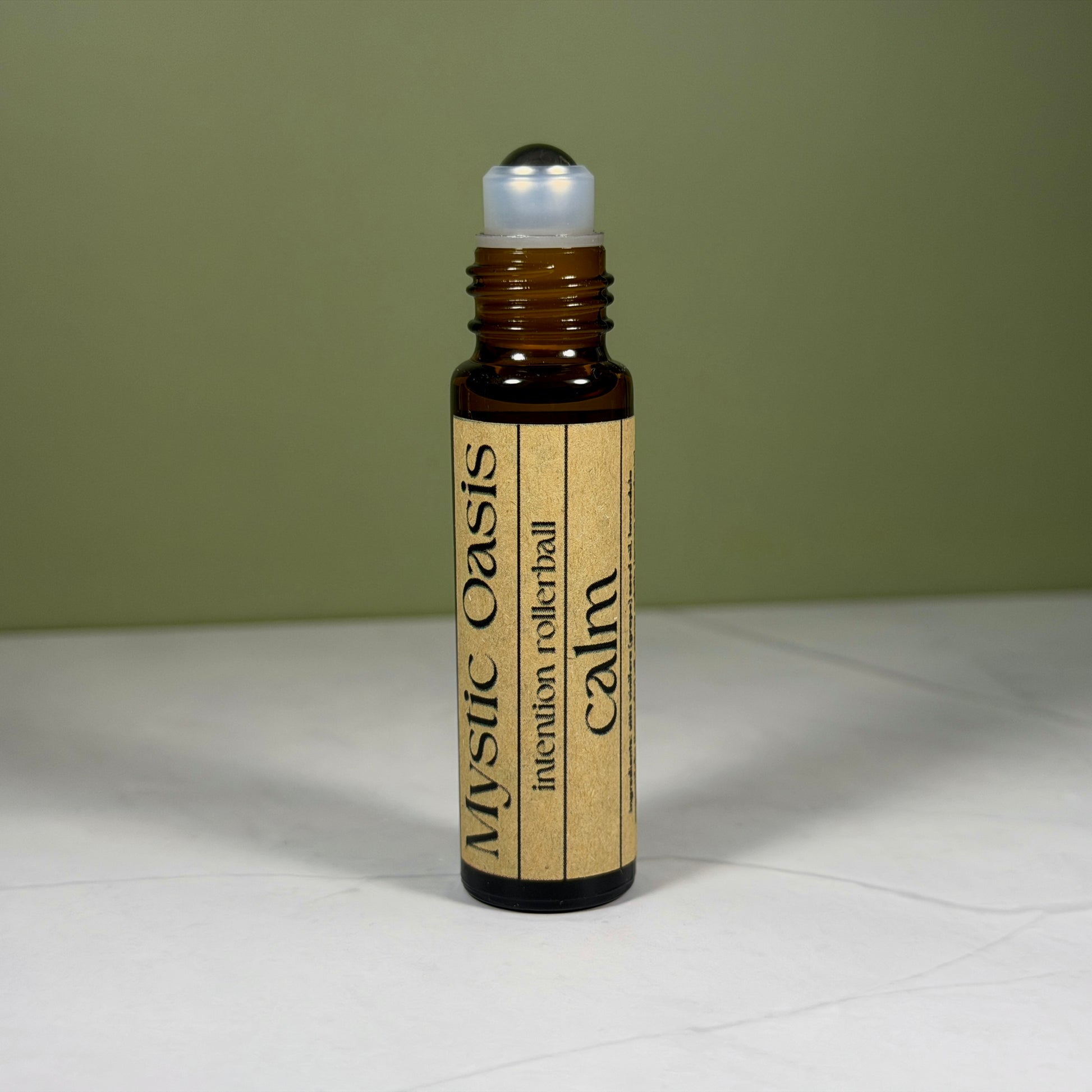 Rollerball bottle labeled 'Calm' by 'Mystic Oasis' on a white surface with a green background