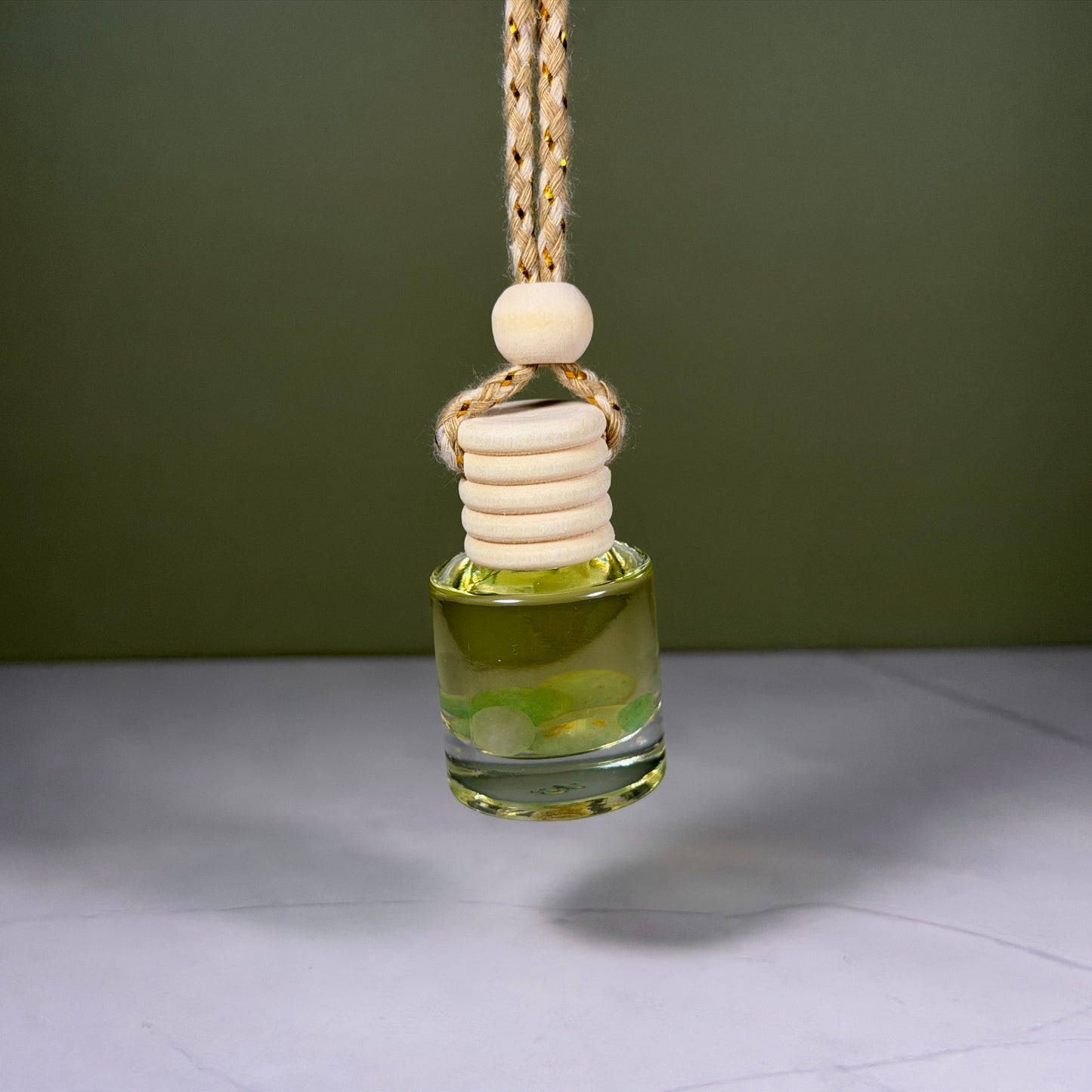 Glass oil diffuser with wooden beads hanging against a green background
