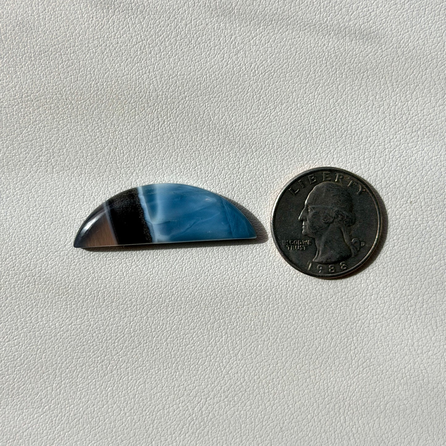 Blue and black half circle stone next to a U.S. quarter on a light gray background