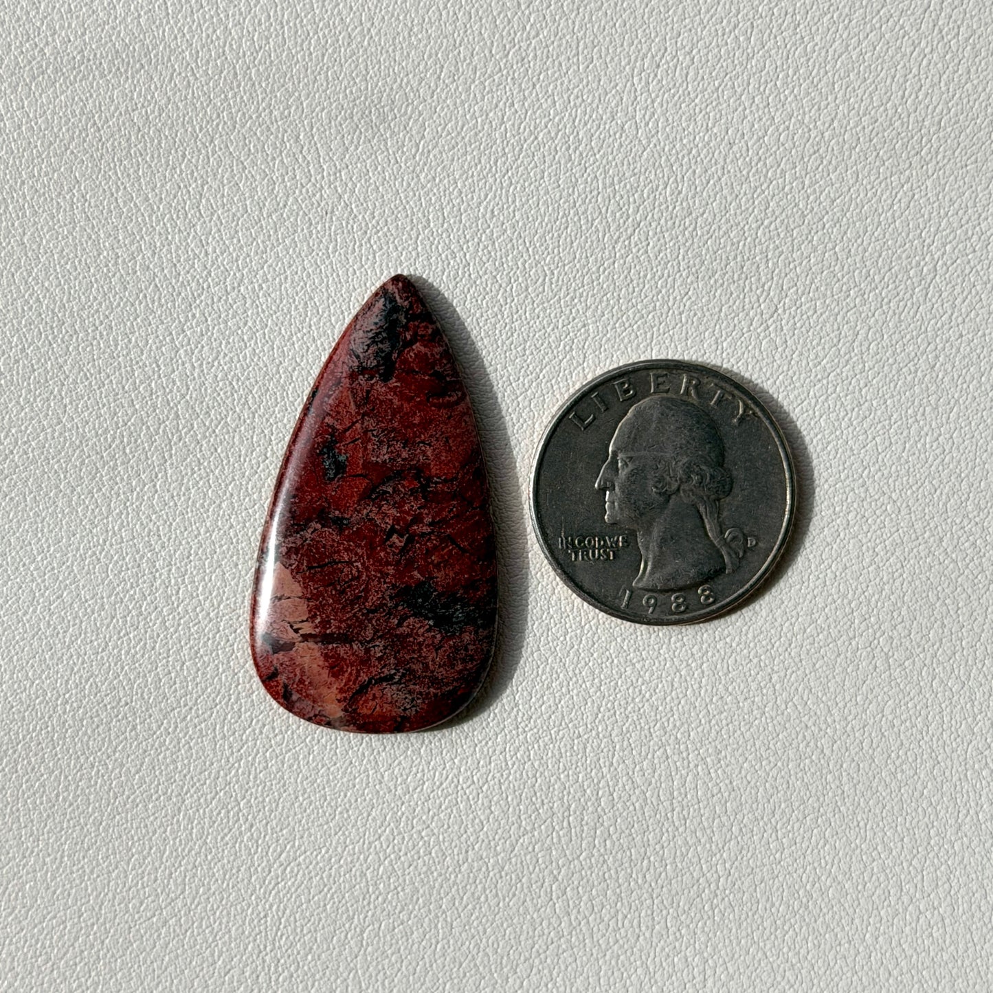 Teardrop-shaped red stone next to a U.S. quarter on a light gray background