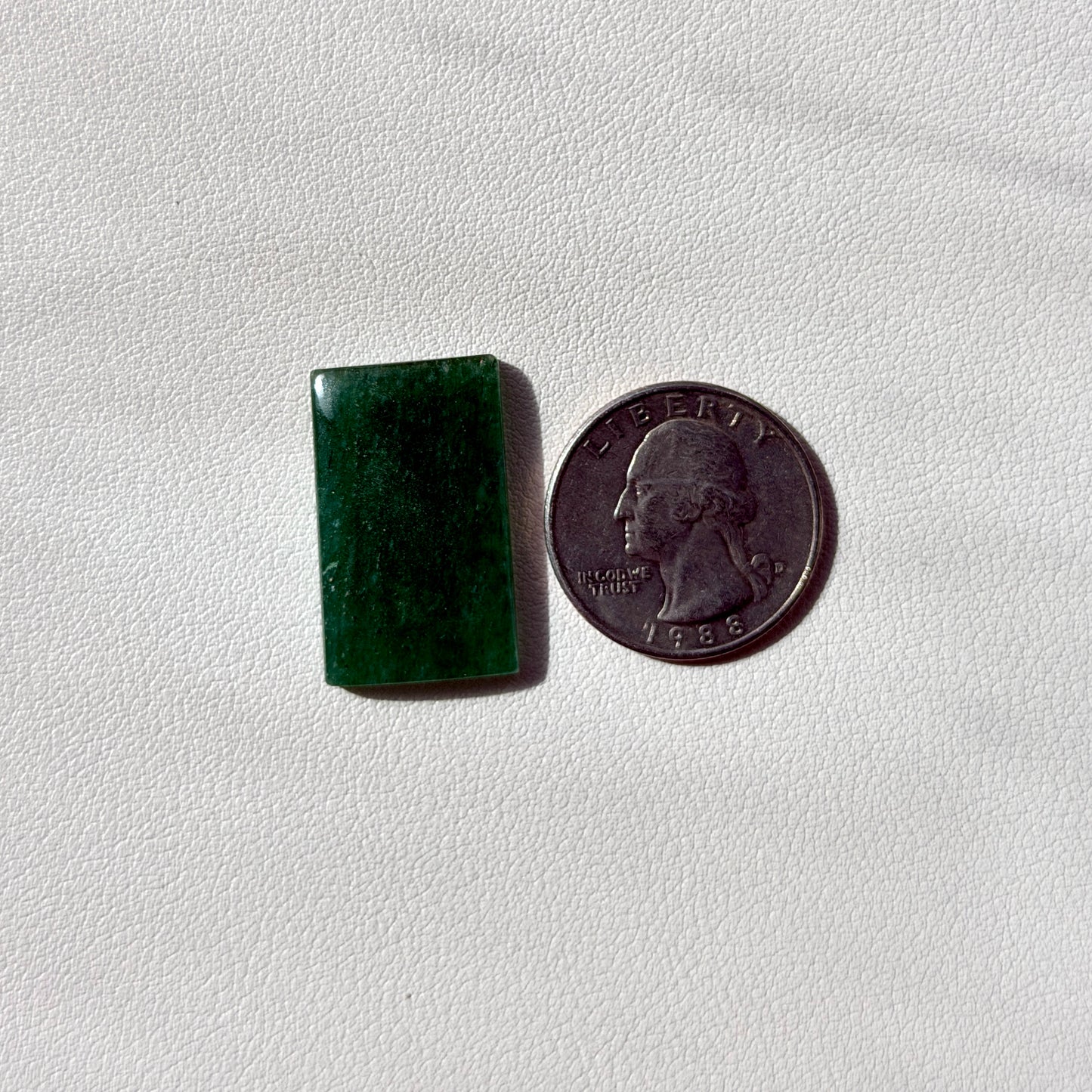 Green rectangular stone next to a U.S. quarter on a white background