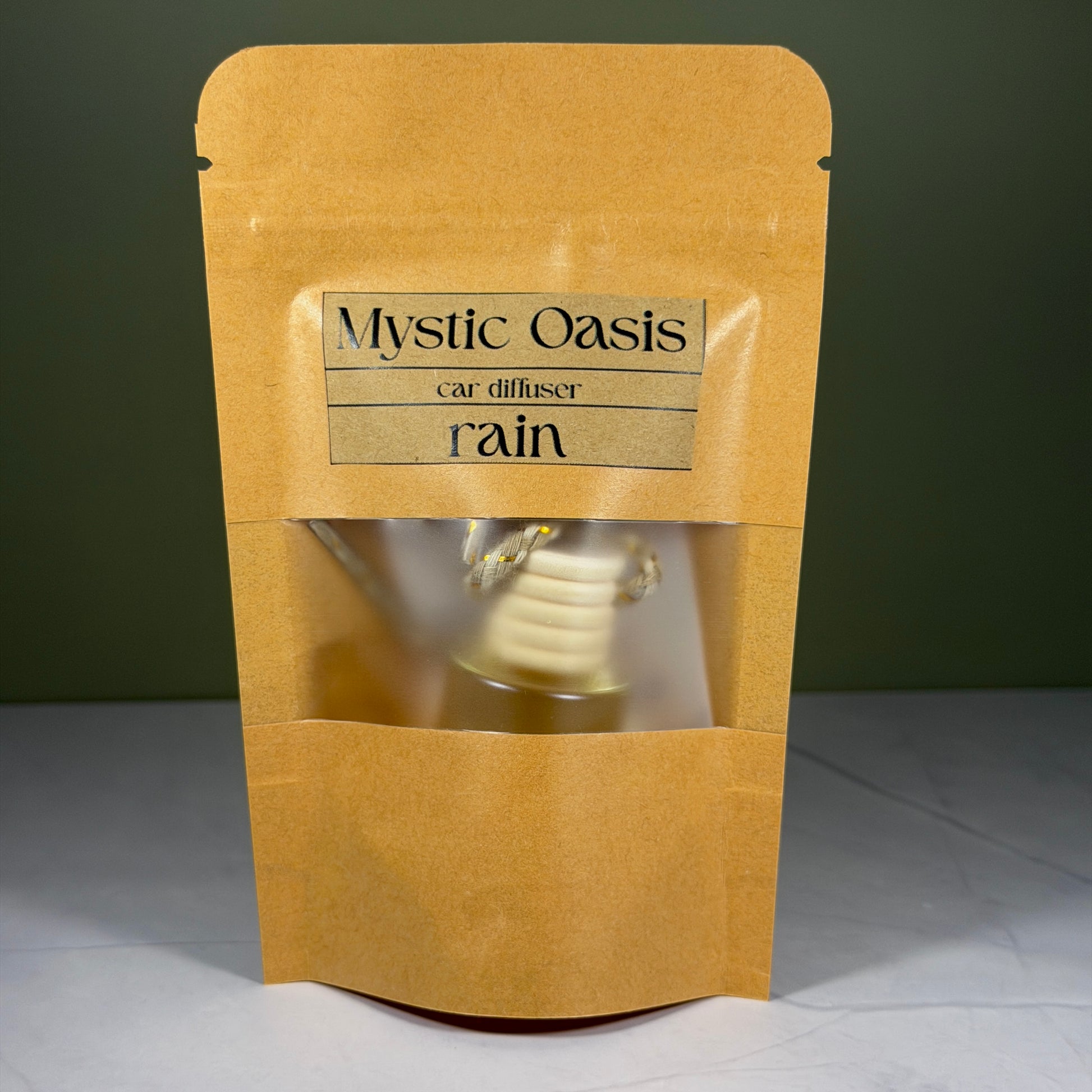 Kraft paper packaging with a car diffuser labeled 'Mystic Oasis rain' on a gray background