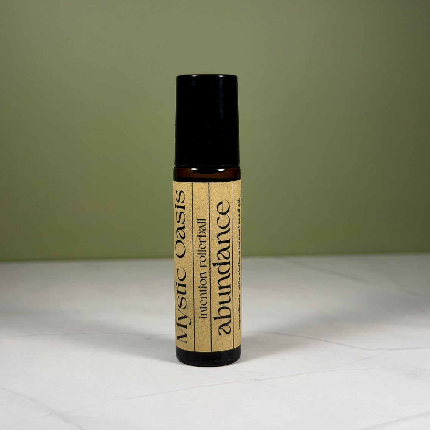 Roll-on bottle labeled 'Mystic Oasis' with 'abundance' on a white surface and green background