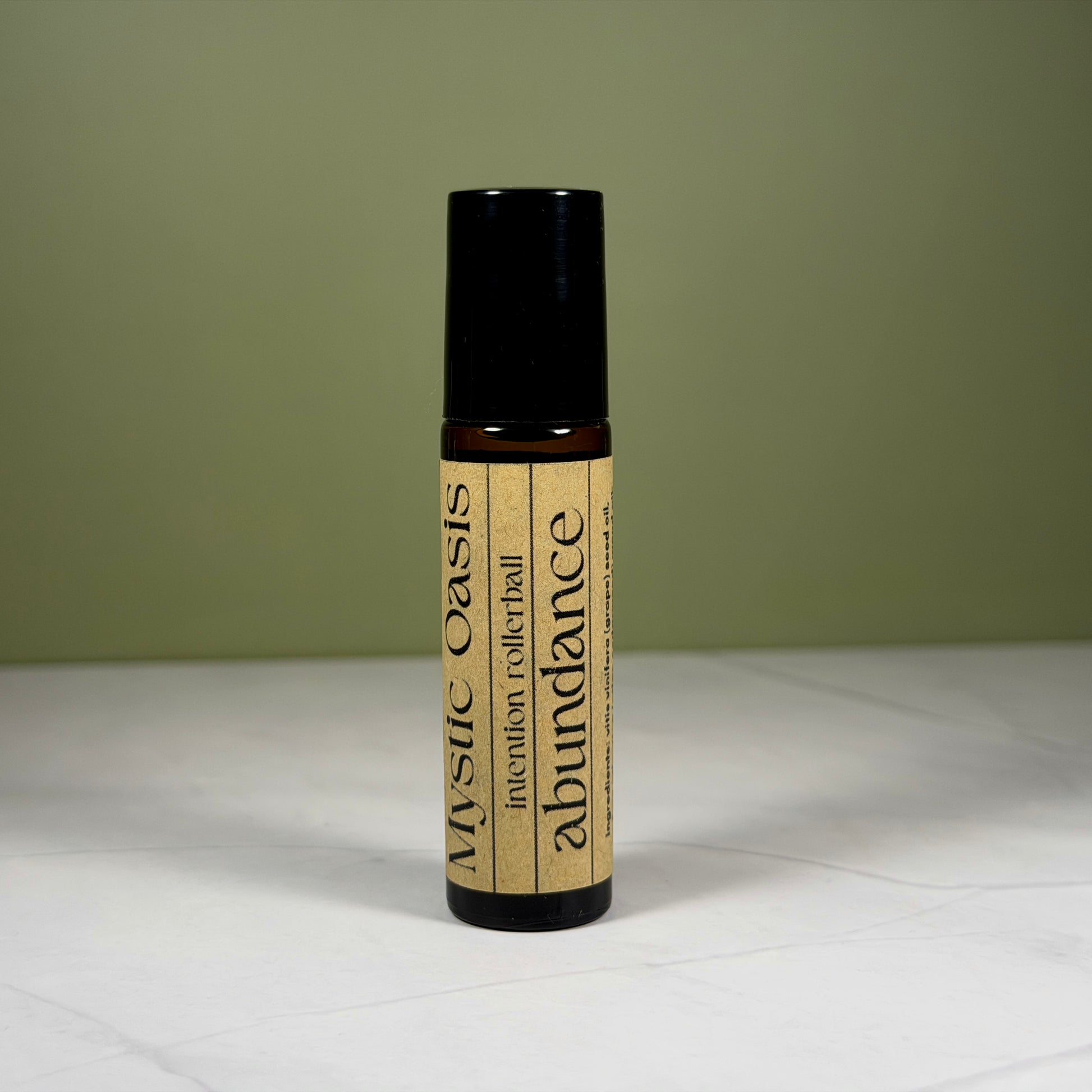 Roll-on bottle labeled 'Mystic Oasis' with 'abundance' on a white surface and green background