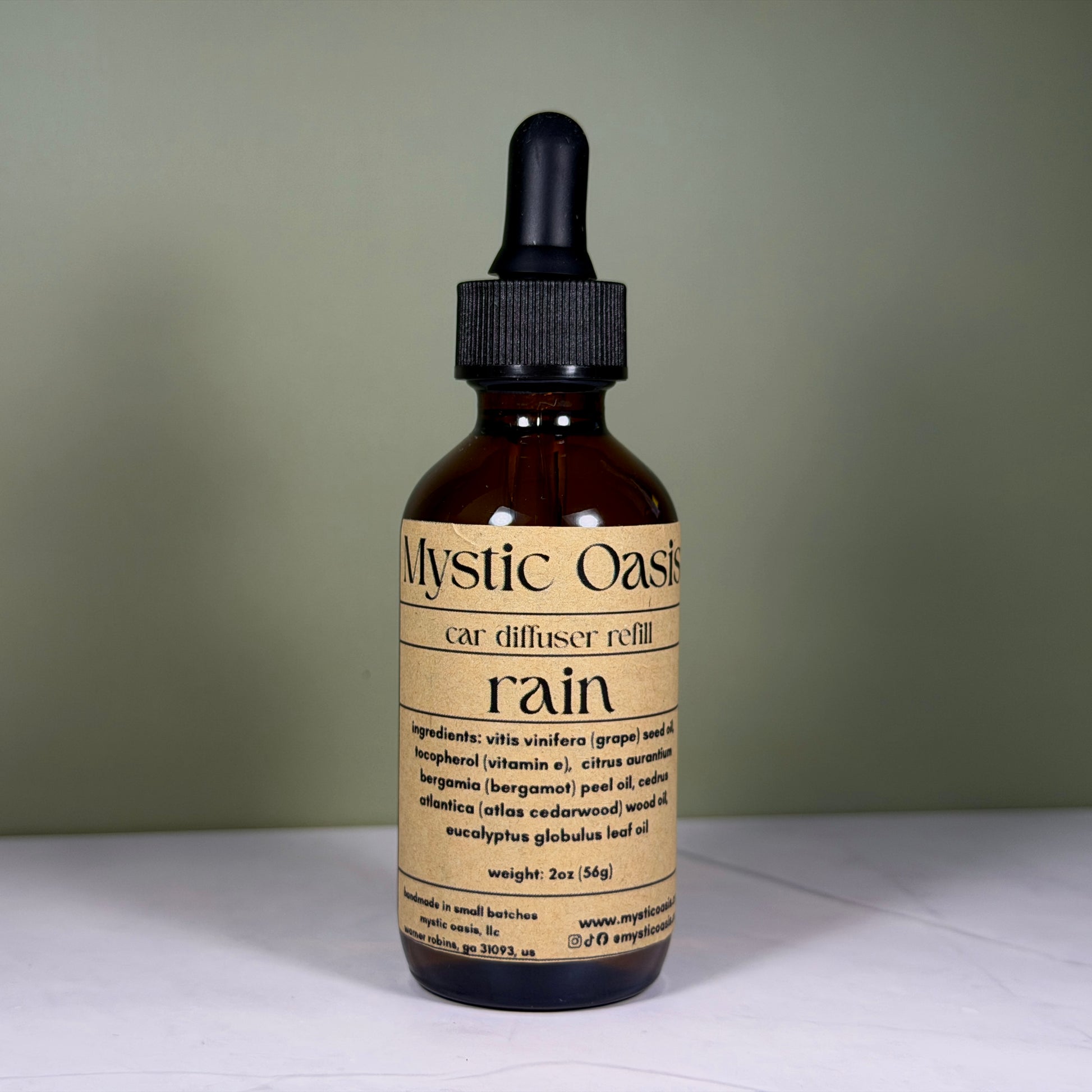 Bottle of Mystic Oasis rain car diffuser refill on a white surface with a green background