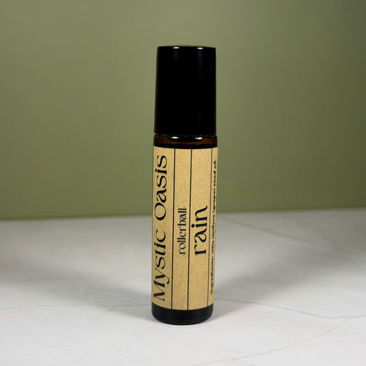 Rollerball bottle labeled 'Mystic Oasis Rain' on a white surface with a green background