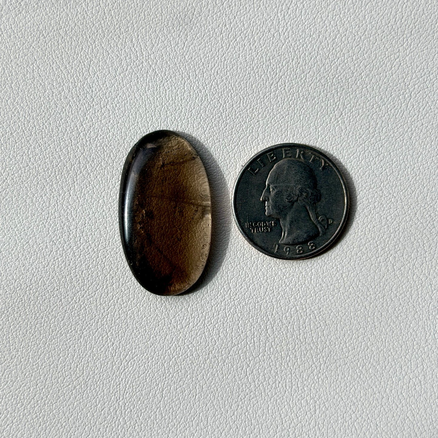 gray oval stone next to a U.S. quarter on a light gray background
