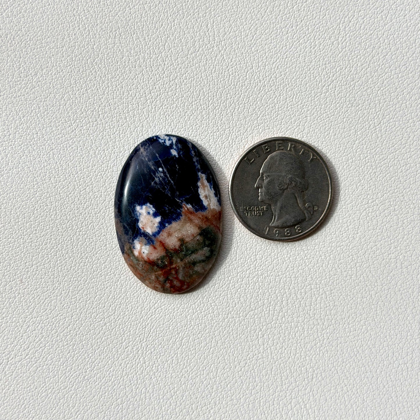 Oval-shaped blue stone next to a U.S. quarter on a light gray background