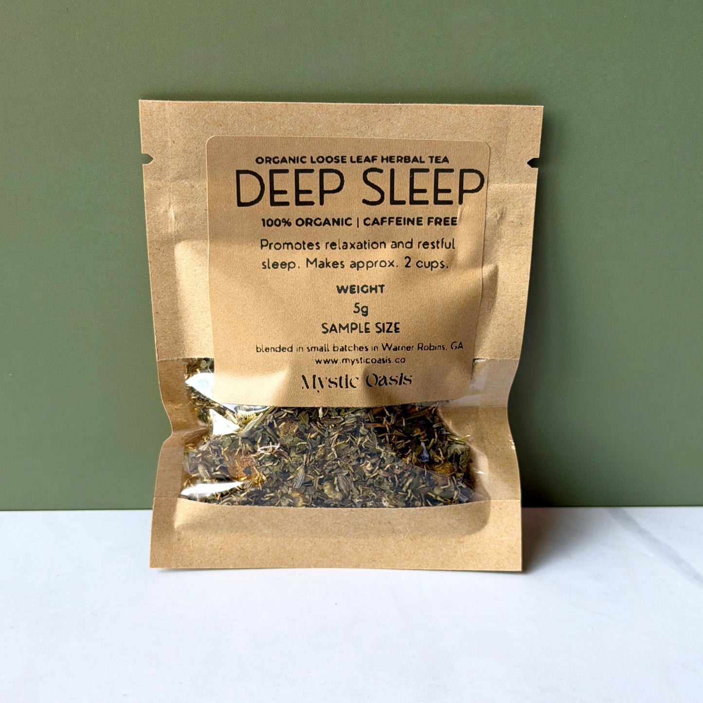 Kraft paper package of 'Deep Sleep' herbal tea with visible tea leaves on a white surface and green background.
